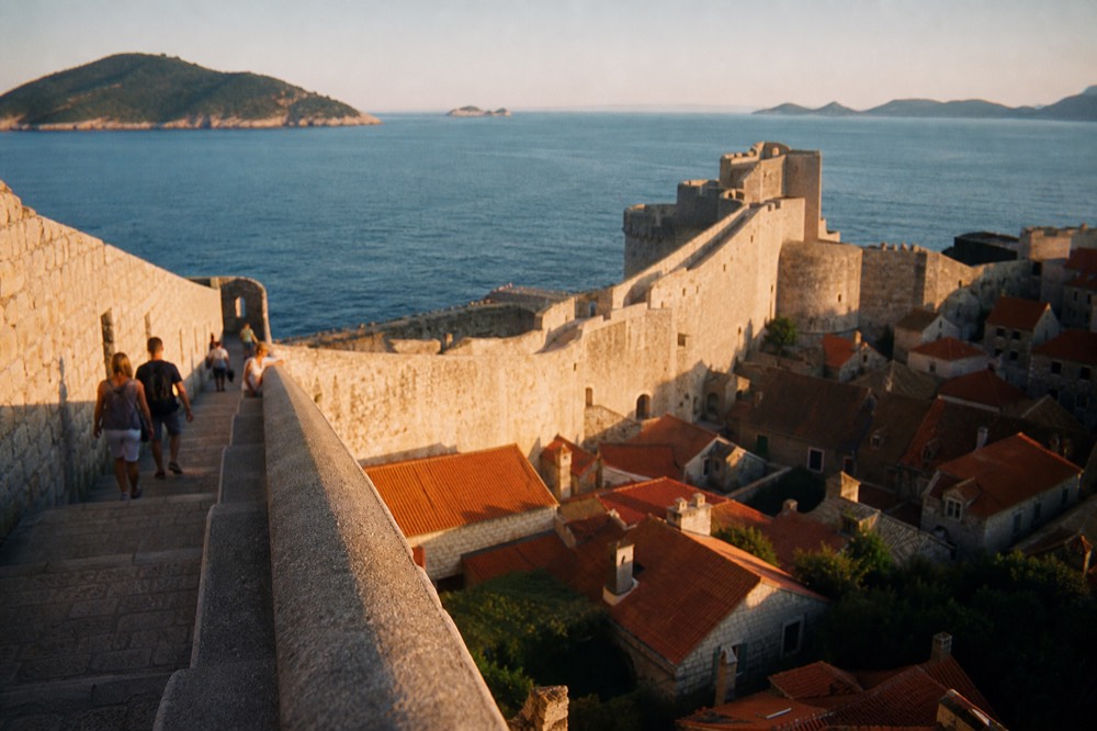 Stone city walls rising above red rooftops with the Adriatic sea beyond