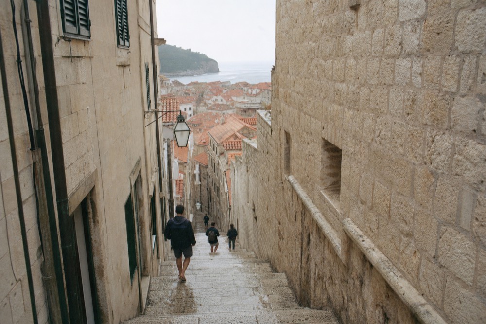 Visitors walking a stone staircase between pale buildings in Dubrovnik old town