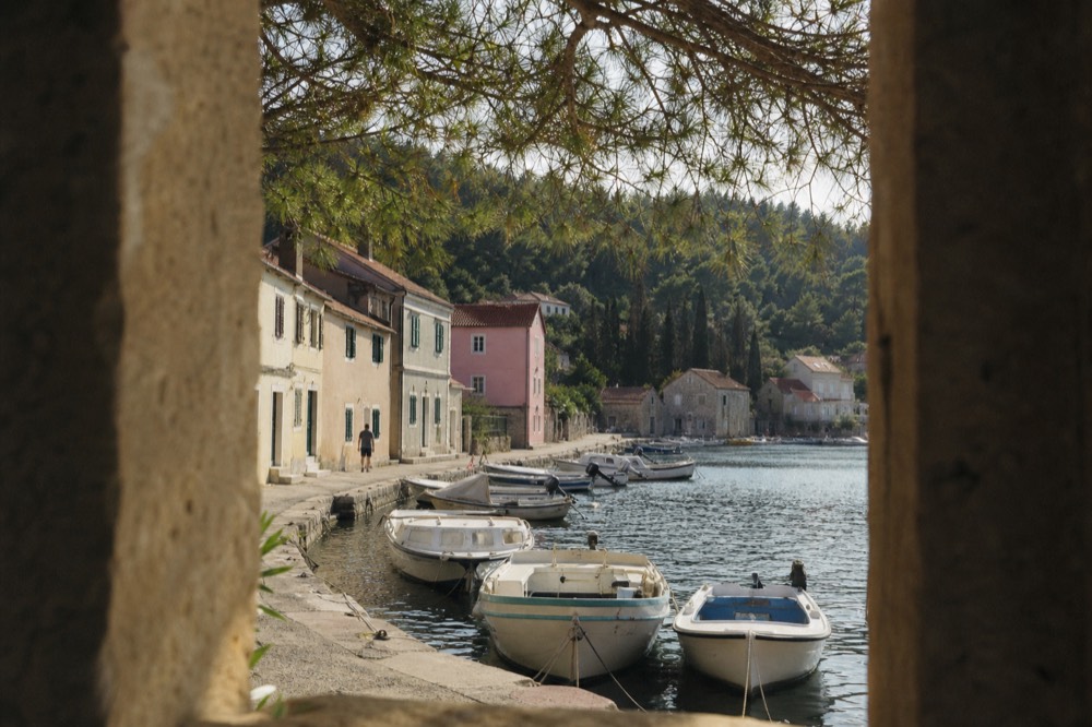 A line of small boats tied along a stone quay in front of pastel island houses