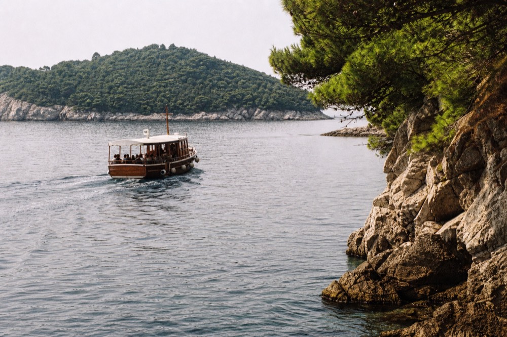A wooden boat cruising past green islands on calm Adriatic water near Dubrovnik