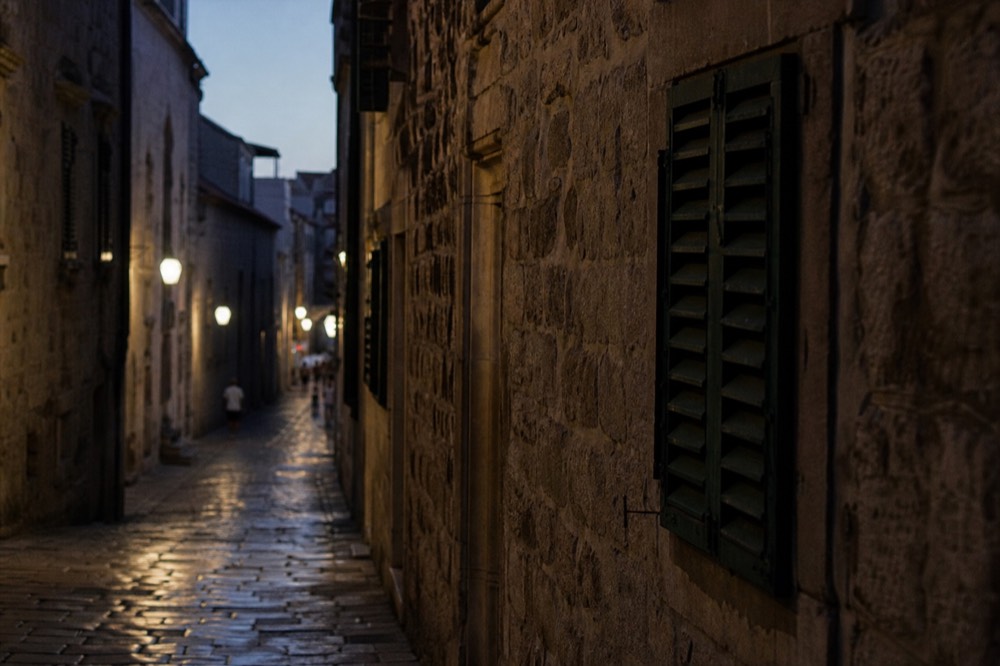 Quiet evening lane inside a walled town with lit stone facades and shutters