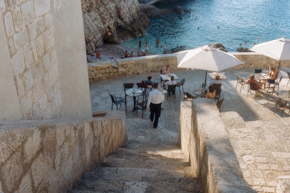 Café tables on a stone square in Dubrovnik with a waiter serving coffee