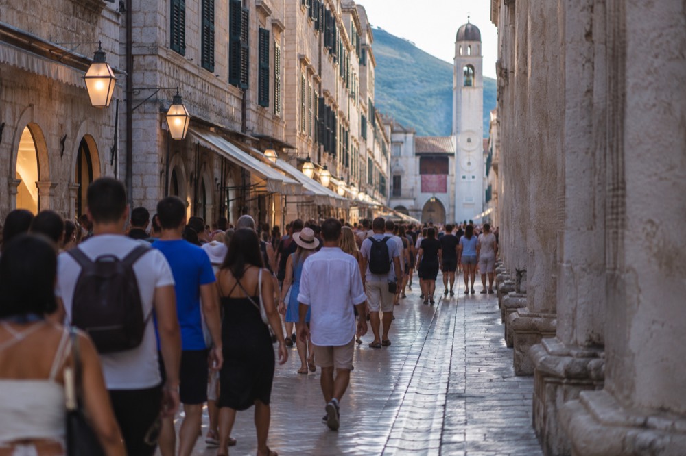 Crowded limestone street with visitors walking between stone buildings in bright sunlight