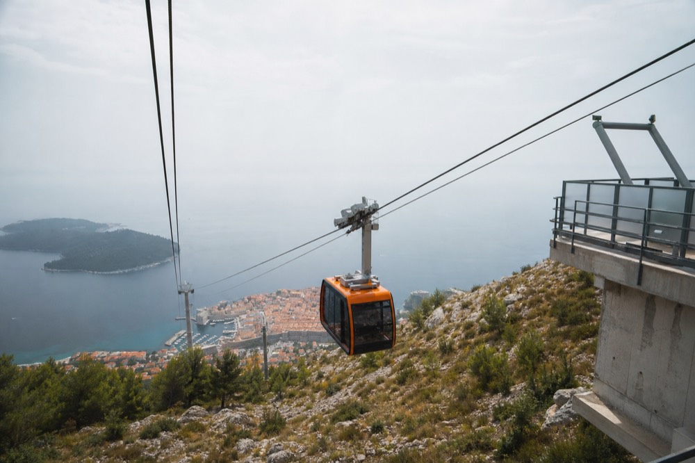 Cable car cabin travelling up a steep hillside toward a summit station above the sea