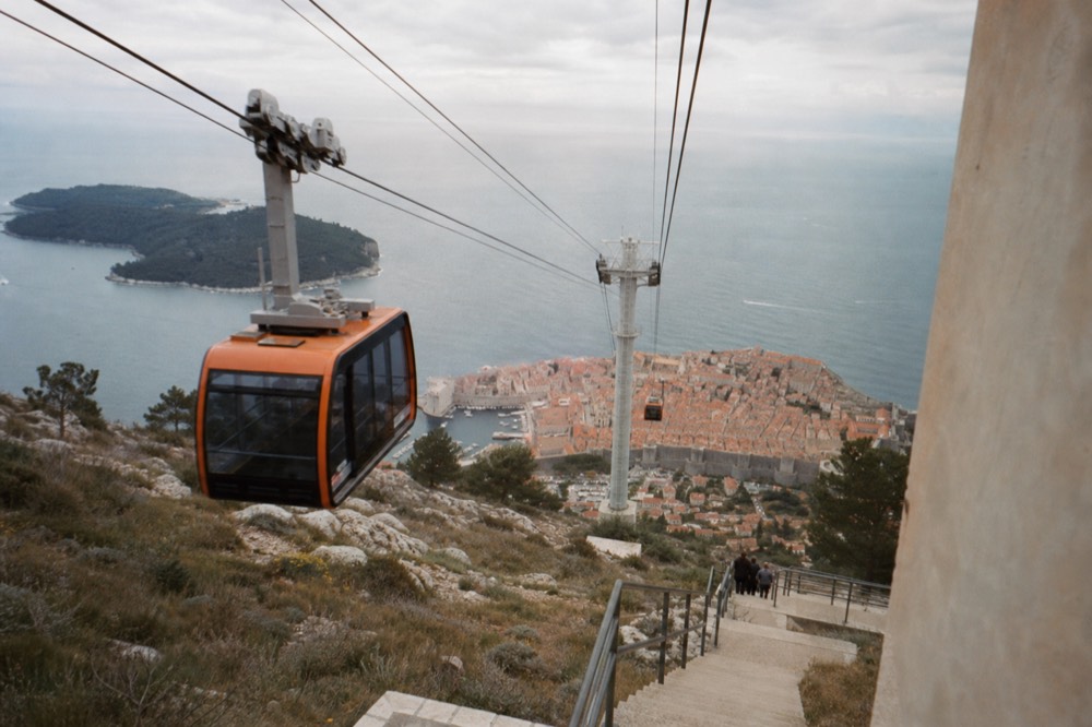 A cable car cabin ascending above red rooftops toward a hilltop station