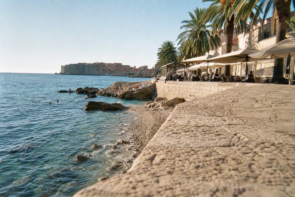 Palm-lined promenade with café terraces along a bay in the late afternoon