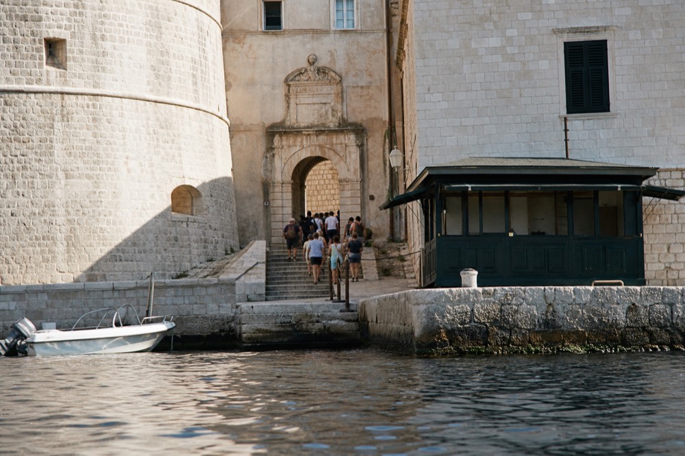 A ticket booth beside a stone city gate with a queue of visitors