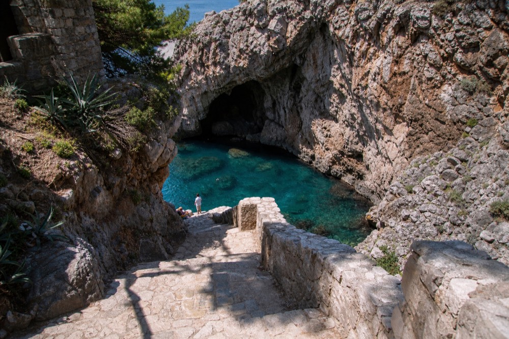 A sea cave entrance with turquoise water at the base of cliffs near Lokrum Island