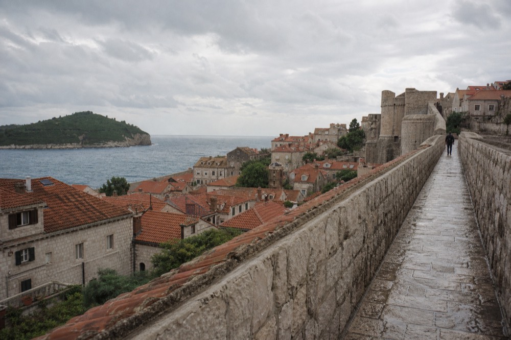 High stone walkway along a fortress wall above red rooftops and the sea