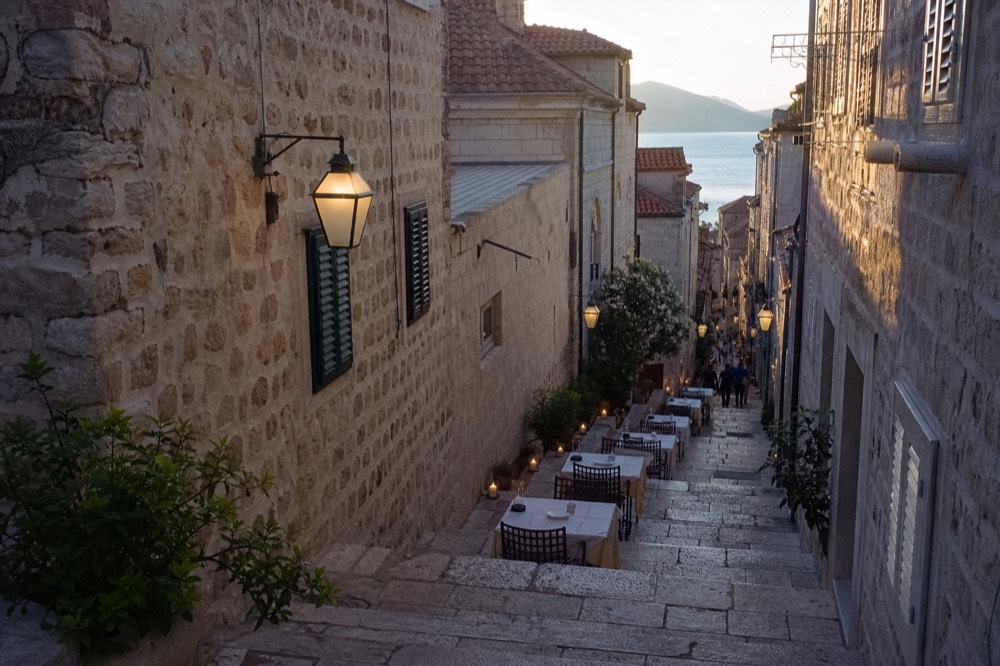 A lantern-lit stone street with restaurant tables set for the evening