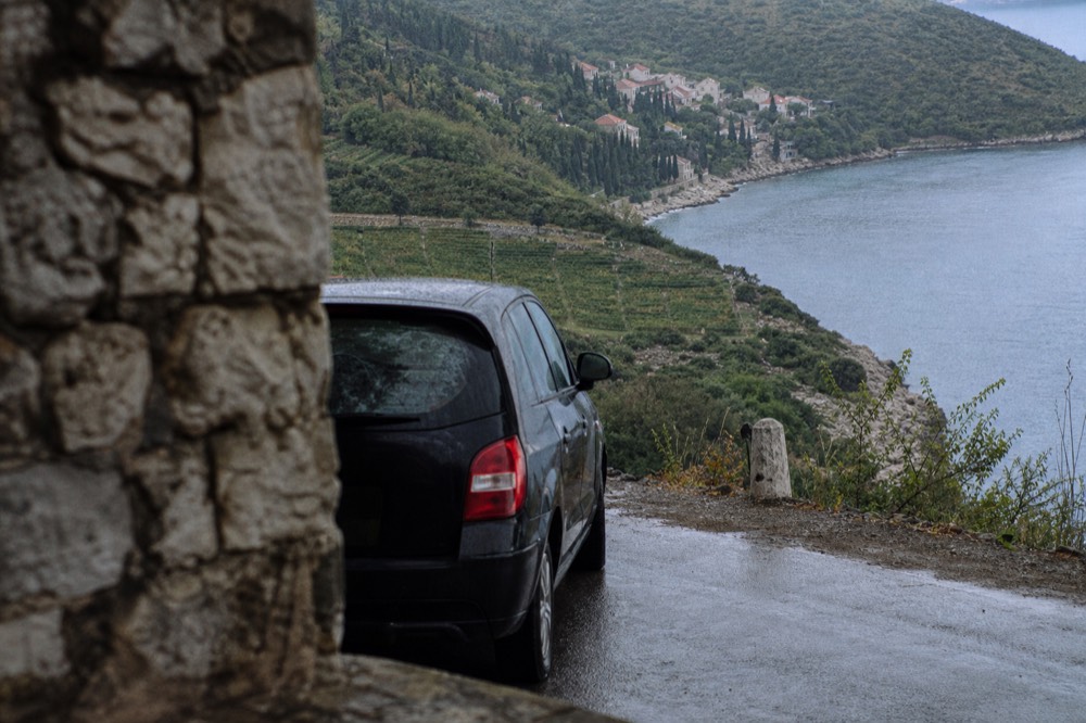 A car parked on a coastal road above a bay with vineyards on the hillside