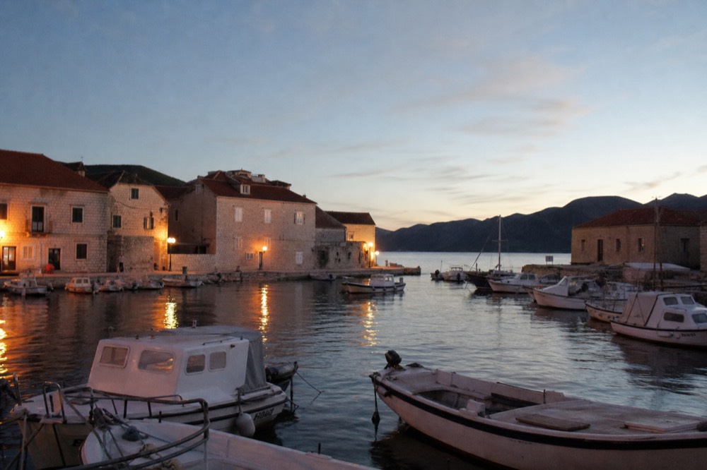 Boats moored in a small harbour at dusk with lights reflecting on calm water