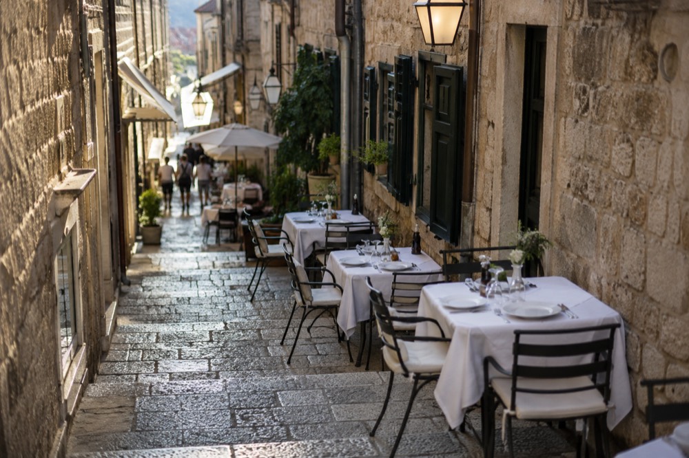 Outdoor cafe tables with white tablecloths set along a narrow stone lane