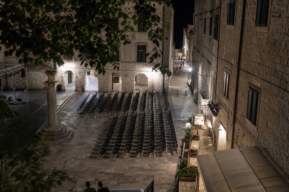 A floodlit stone courtyard in Dubrovnik at night with empty rows of chairs set out for a performance
