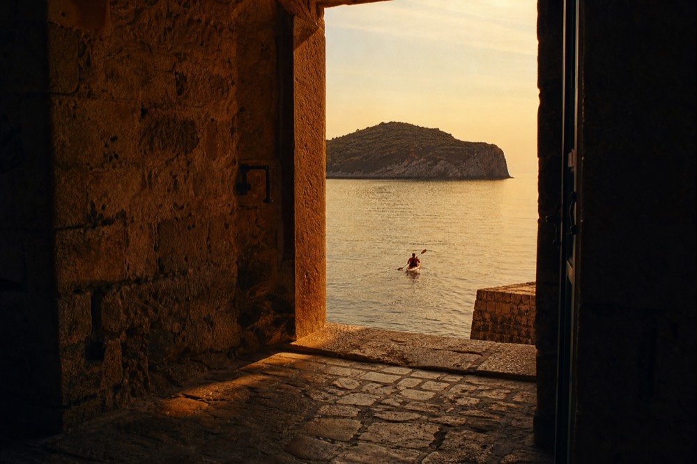 A person paddling a kayak across calm golden water toward a rocky island