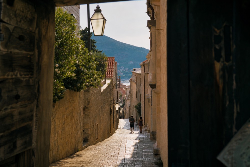 A narrow stone street inside a walled town lit by warm low sun with long shadows