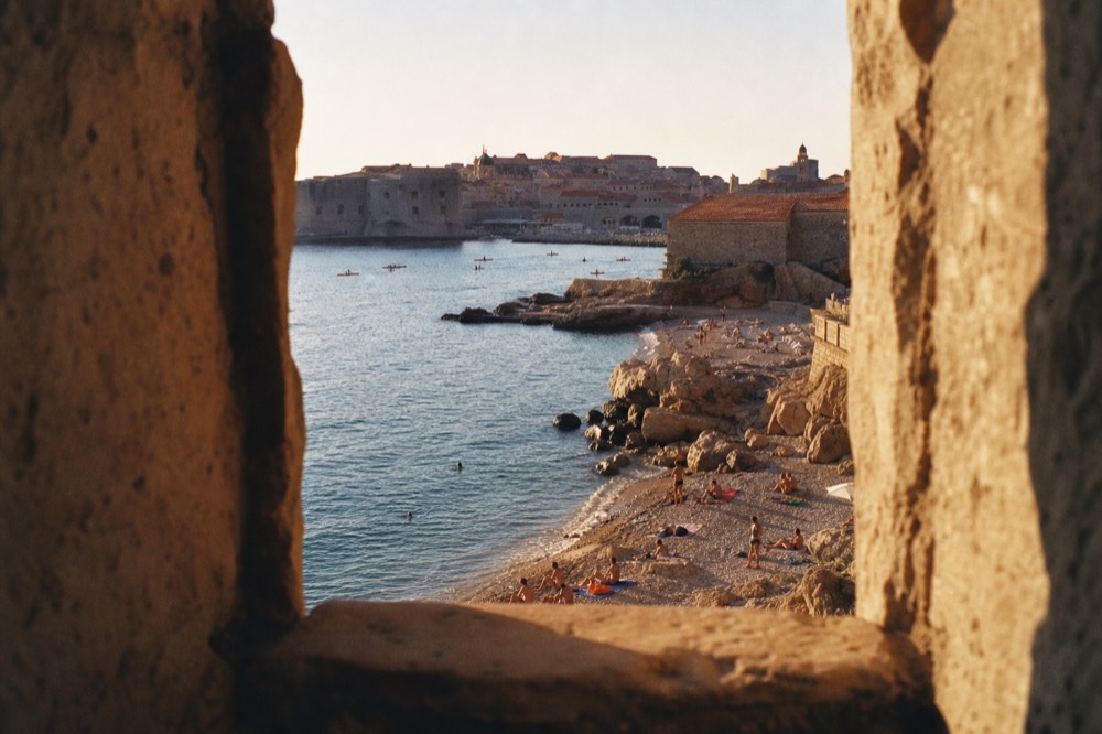 Golden evening light on a calm pebble cove with the walled city glowing across the bay
