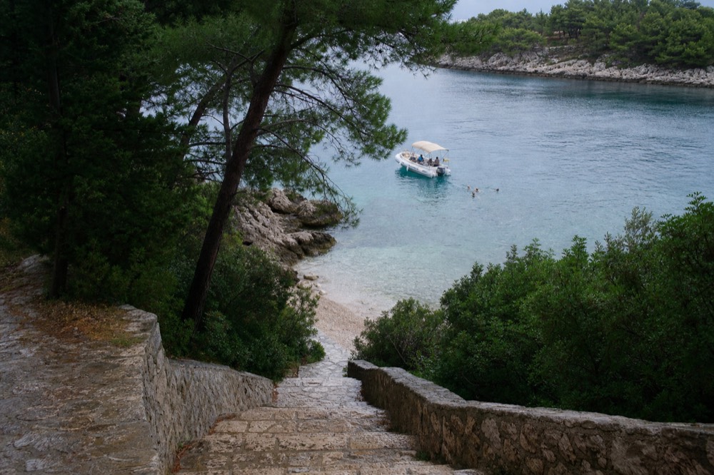 Boat anchored in a quiet island cove with swimmers in the water near a pebble shore