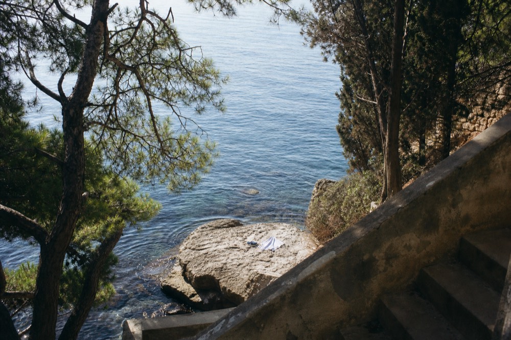 Towel and water shoes on a flat rock beside calm morning sea