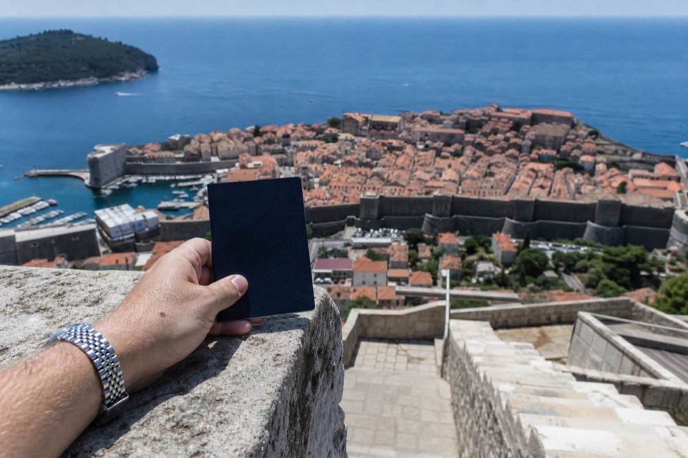 Passport held above a stone wall with the walled city of Dubrovnik below