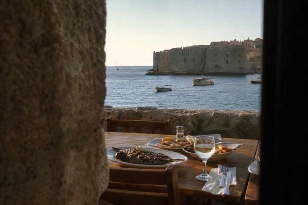 Plates of grilled fish and seafood on a restaurant table beside a stone wall
