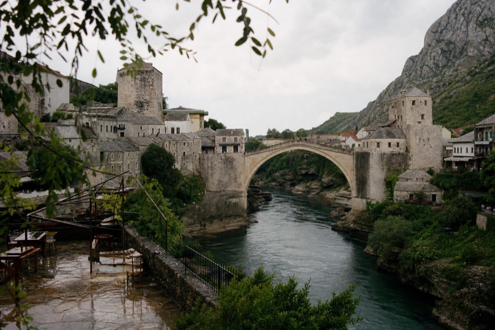Old stone bridge arching over a river in Mostar with hills behind