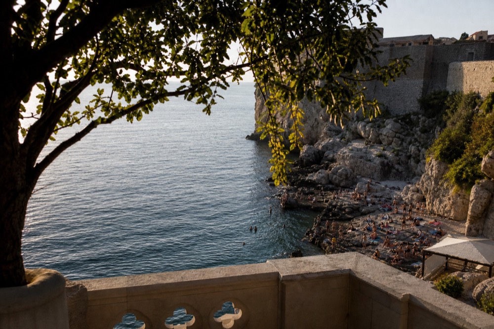 Swimmers on a rocky beach below Dubrovnik's walls at sunset