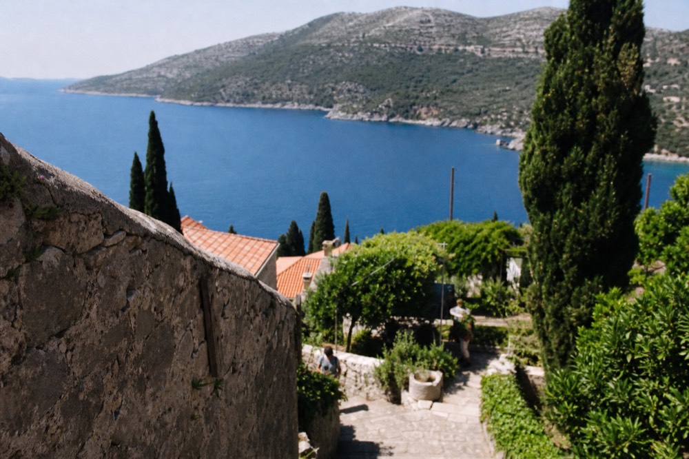 Terraced stone gardens with tall cypress trees sloping toward a calm bay