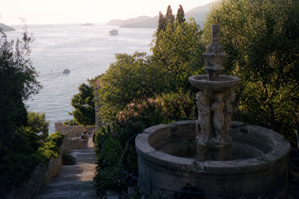 A large stone fountain with carved figures surrounded by dense green foliage