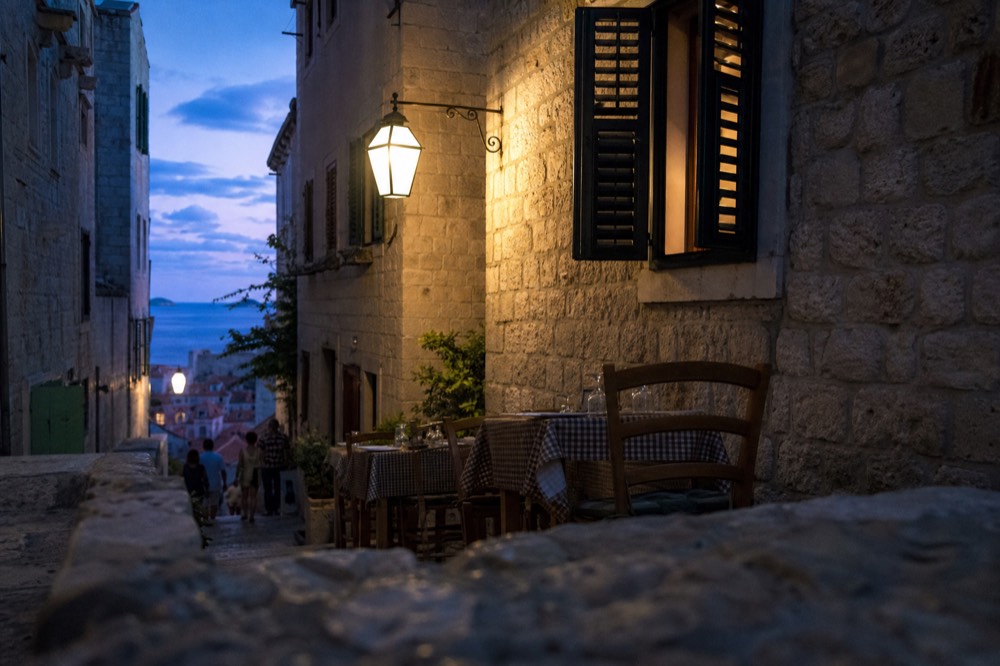 A narrow side street in Dubrovnik's Old Town with a quiet konoba terrace, away from the crowded main street.