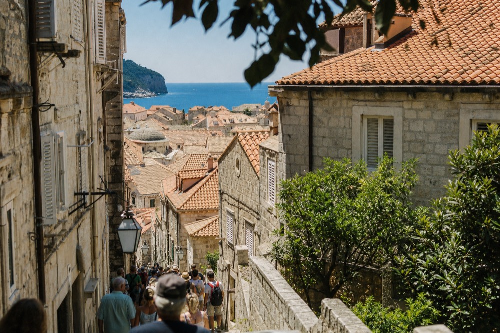A crowded narrow stone street in an old town with tour groups walking
