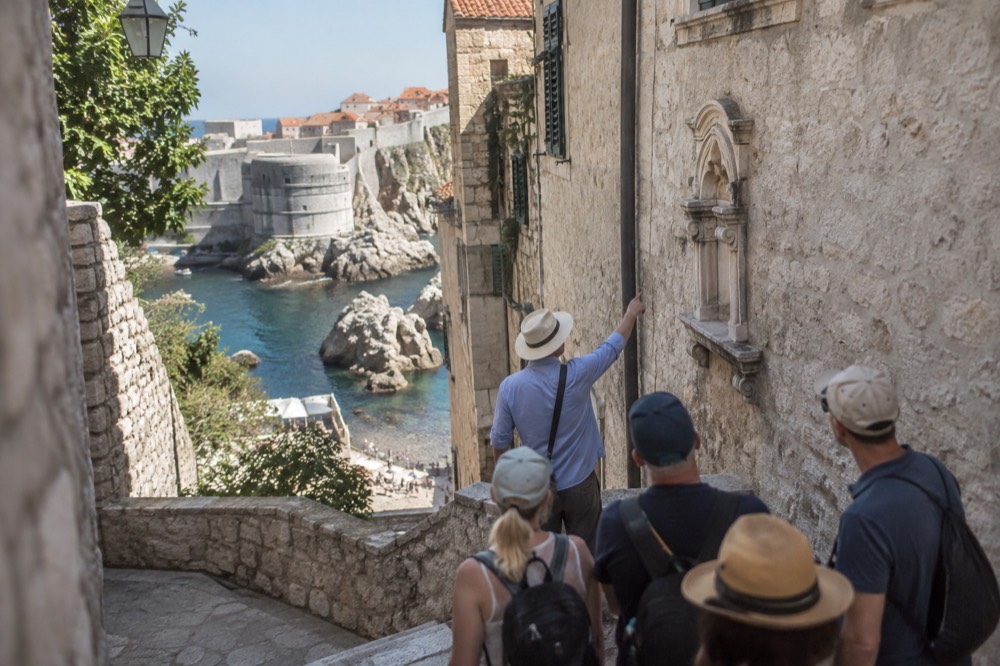A guide pointing out a building detail to a small group on a Dubrovnik street