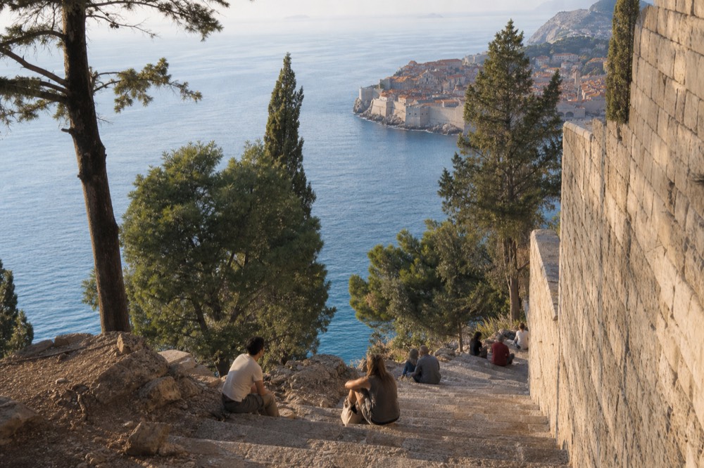 Visitors resting on stone steps below Dubrovnik city walls in sunshine