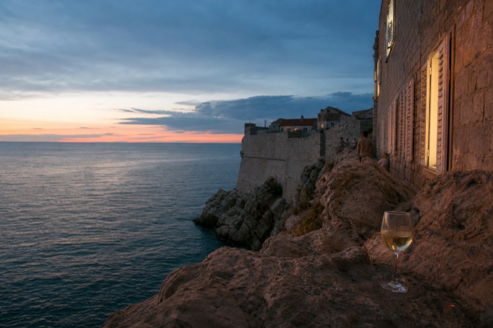 A drink on a rocky ledge outside the city walls above the open sea at sunset