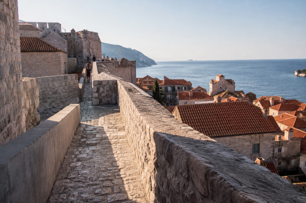 Walking path on top of city walls with red rooftops and the sea beyond