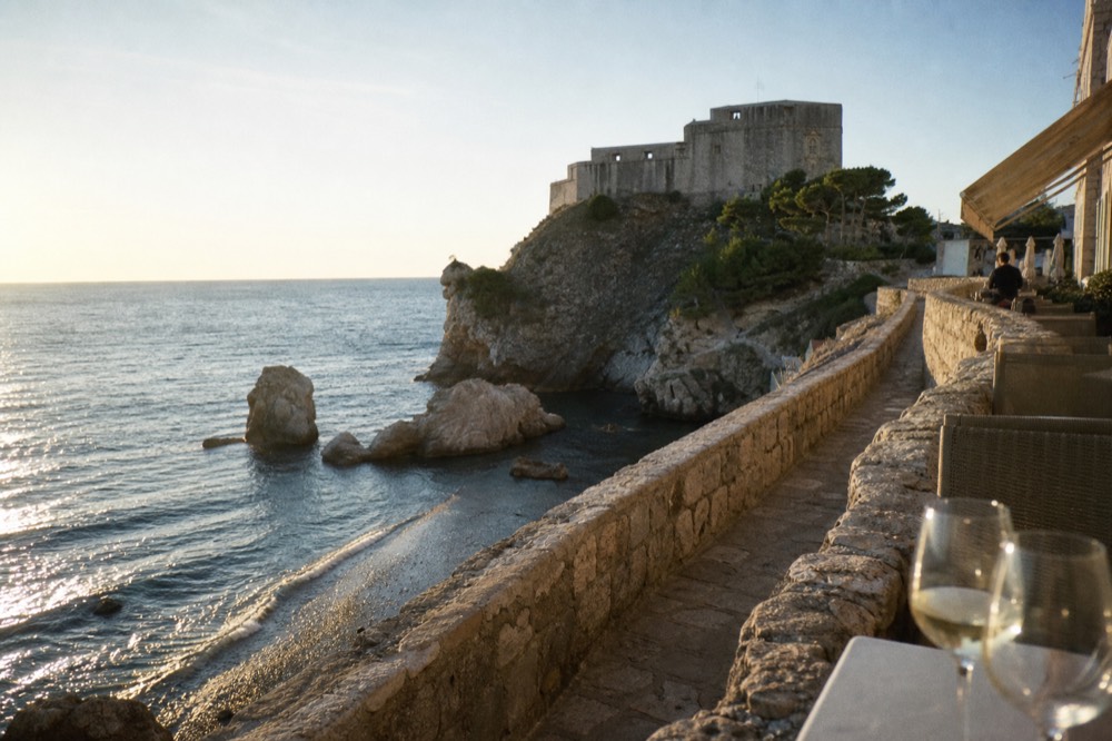 A terrace table with wine glasses overlooking the sea at golden hour