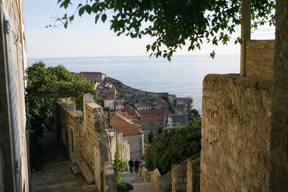 The city walls of Dubrovnik curving above red rooftops with the Adriatic Sea beyond