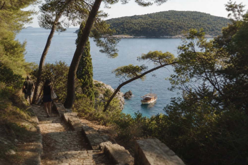 A wooden boat anchored in a sheltered cove beside a green Adriatic island