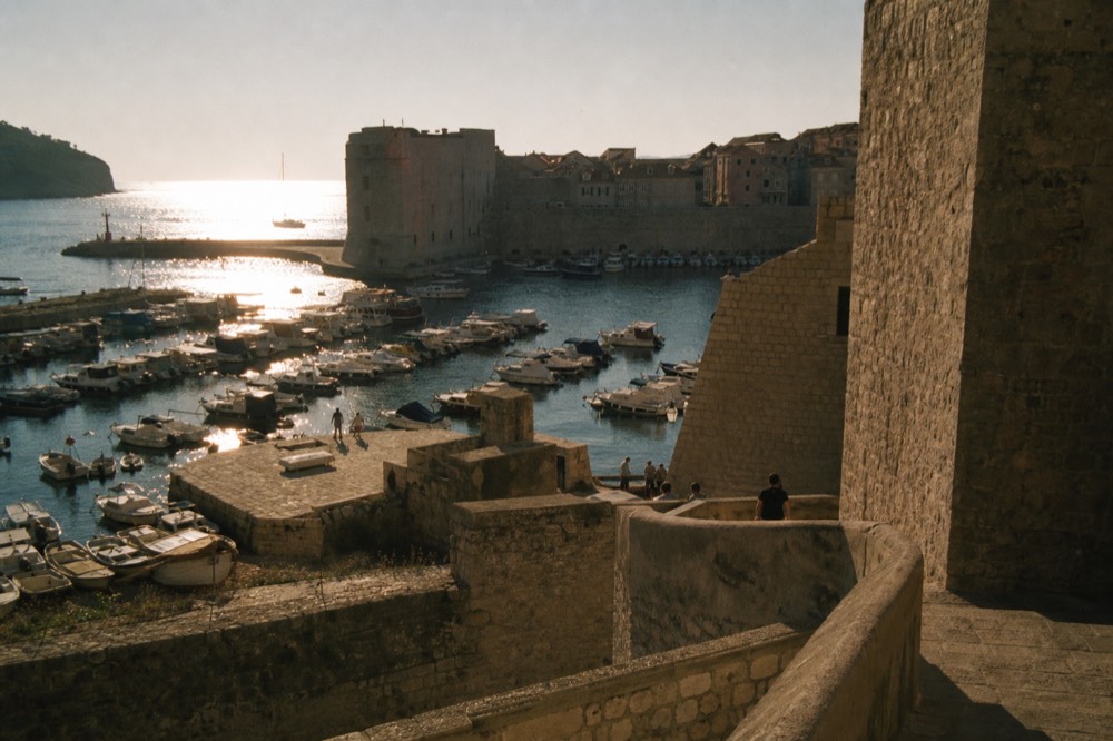 The Old Town harbour of Dubrovnik at sunset with boats moored beside the city walls