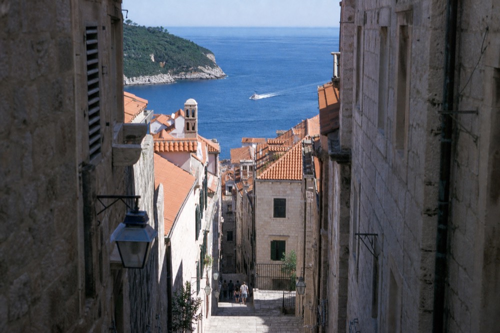 A narrow shaded stone lane with worn steps between tall old buildings