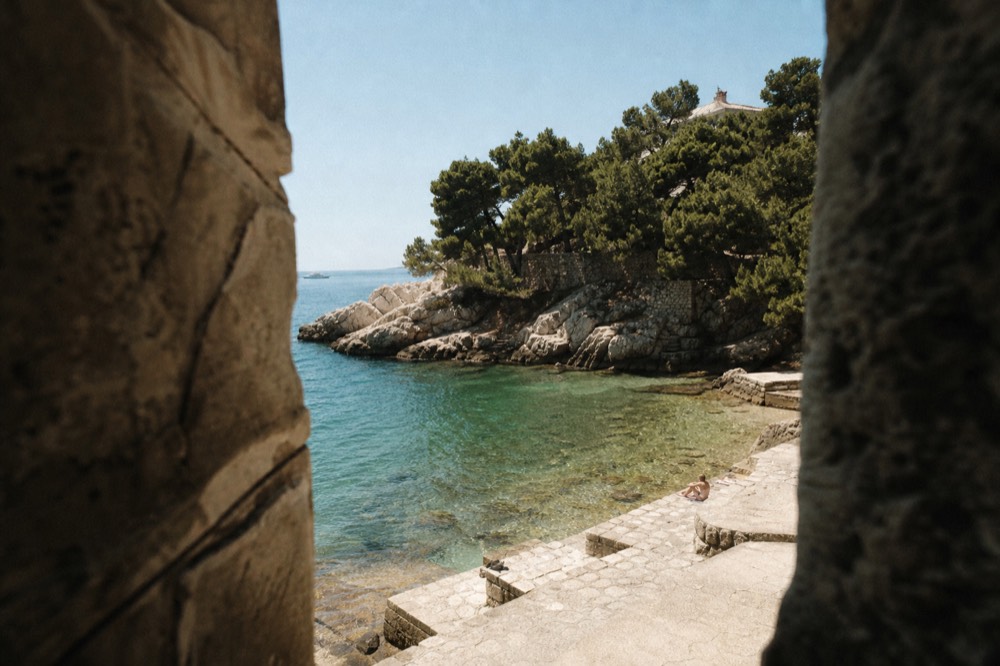 A calm sheltered swimming bay with clear shallow water and pine trees at the shoreline