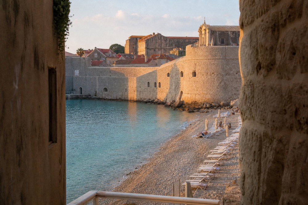 A pebble beach with calm turquoise water and sun loungers along the shoreline